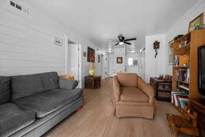 Living area featuring wood finished floors, a ceiling fan, and wooden walls