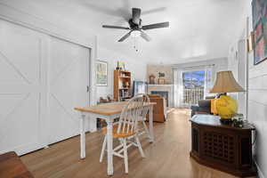 Dining area with light wood-type flooring, a brick fireplace, wood walls, and ceiling fan
