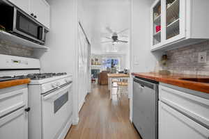 Kitchen featuring appliances with stainless steel finishes, white cabinetry, butcher block counters, glass insert cabinets, and tasteful backsplash