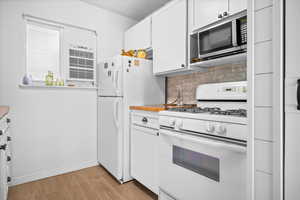 Kitchen featuring white appliances, white cabinetry, tasteful backsplash, light wood-type flooring, and a wall unit AC