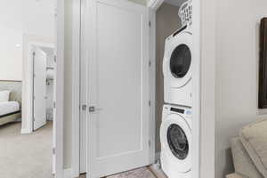 Washroom with stacked washing machine and dryer and light colored carpet