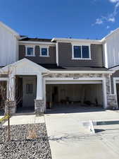 View of front facade featuring stone siding, concrete driveway, board and batten siding, and an attached garage