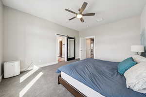 Carpeted bedroom with a barn door and ceiling fan