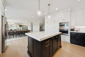 Kitchen with dark cabinetry, appliances with stainless steel finishes, light wood-style flooring, recessed lighting, and open floor plan