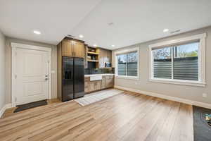 Kitchen with black refrigerator with ice dispenser, decorative backsplash, light countertops, open shelves, and light wood-style floors