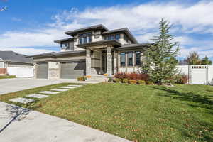 Prairie-style home with stucco siding, concrete driveway, a gate, an attached garage, and stone siding