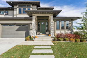 Doorway to property with stucco siding, driveway, a lawn, an attached garage, and stone siding