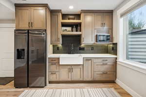 Kitchen with black fridge, open shelves, light wood-type flooring, decorative backsplash, and stainless steel microwave