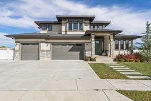Prairie-style house with stone siding, stucco siding, driveway, a garage, and a front lawn