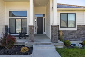 Entrance to property with stone siding, a porch, and a shingled roof