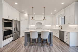 Kitchen with appliances with stainless steel finishes, hanging light fixtures, white cabinets, light wood-type flooring, and a center island