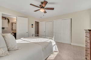 Bedroom featuring light colored carpet, multiple closets, connected bathroom, and ceiling fan