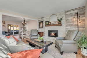 Living area with wood finished floors, wood walls, a fireplace, a chandelier, and an accent wall