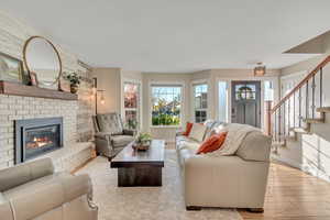 Living room featuring light wood-style floors, stairs, and a brick fireplace