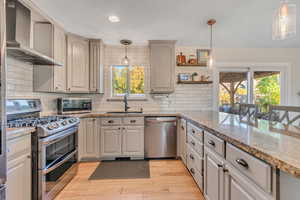 Kitchen featuring pendant lighting, appliances with stainless steel finishes, wall chimney range hood, decorative backsplash, and recessed lighting