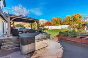Fenced backyard featuring an outdoor hangout area, a deck with mountain view, a gazebo, a hot tub, and a garden