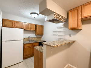 Kitchen featuring freestanding refrigerator, a textured ceiling, light stone countertops, a kitchen bar, and tasteful backsplash