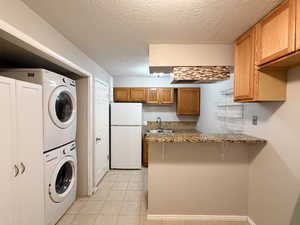 Laundry area with a textured ceiling, light tile patterned floors, and stacked washer / dryer