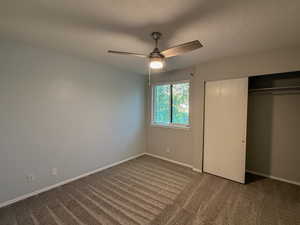 Unfurnished bedroom featuring carpet flooring, a ceiling fan, a closet, and a textured ceiling