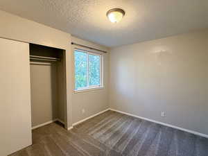 Unfurnished bedroom with dark carpet, a textured ceiling, and a closet