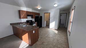 Kitchen with black appliances, dark countertops, independent washer and dryer, a peninsula, and under cabinet range hood