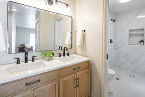 Full bath with double vanity and a marble finish shower