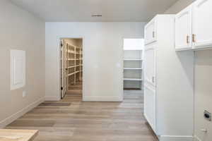 Kitchen featuring white cabinets, light wood finished floors, a textured ceiling, and electric panel