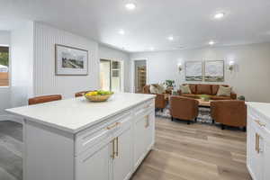 Kitchen with white cabinets, light wood-style floors, recessed lighting, light stone counters, and a kitchen island