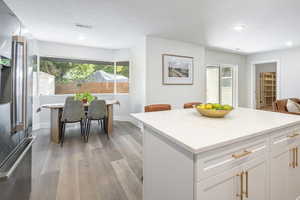 Kitchen featuring stainless steel fridge with ice dispenser, white cabinetry, light wood-type flooring, light stone counters, and a kitchen island