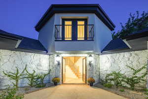 View of exterior entry with stone siding, stucco siding, and roof with shingles