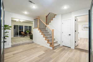 Foyer entrance with a textured ceiling, stairway, and light wood-style flooring