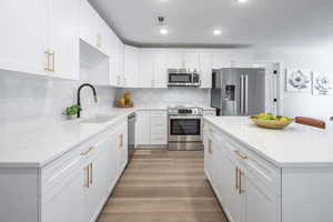 Kitchen featuring stainless steel appliances, backsplash, white cabinets, light wood-style floors, and recessed lighting