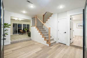 Entryway featuring a textured ceiling, stairs, and light wood-type flooring