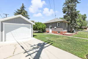 View of front of property with a front lawn, concrete driveway, brick siding, an outbuilding, and a detached garage