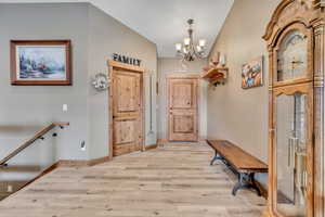 Entryway with a chandelier, light wood-style floors, and vaulted ceiling