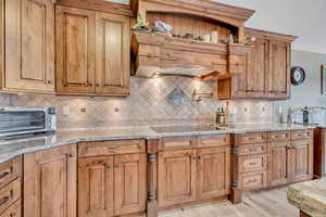 Kitchen featuring light stone counters, under cabinet range hood, tasteful backsplash, and brown cabinets