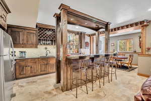 Indoor wet bar with appliances with stainless steel finishes, light stone countertops, backsplash, recessed lighting, and brown cabinets