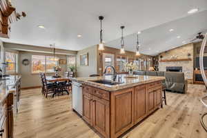 Kitchen featuring brown cabinets, decorative light fixtures, light stone countertops, an island with sink, and lofted ceiling