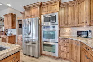 Kitchen with tasteful backsplash, appliances with stainless steel finishes, brown cabinets, and recessed lighting