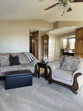 Living room featuring a textured ceiling, carpet flooring, ceiling fan, and lofted ceiling