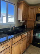 Kitchen featuring brown cabinets, black appliances, dark stone counters, and light tile patterned flooring