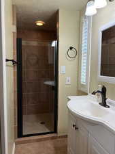 Full bathroom featuring vanity, light tile patterned floors, a shower stall, and a textured ceiling