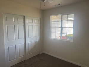 Unfurnished bedroom with dark carpet, a closet, and a ceiling fan