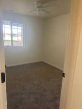 Empty room featuring dark colored carpet and a ceiling fan