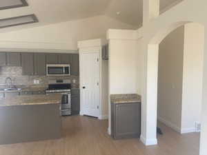 Kitchen with stainless steel appliances, dark wood finished floors, arched walkways, vaulted ceiling, and light stone counters