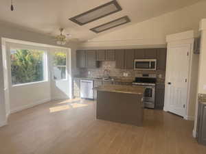 Kitchen with stainless steel appliances, tasteful backsplash, lofted ceiling, a kitchen island, and light wood-style flooring