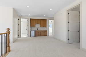 Kitchen featuring brown cabinetry, backsplash, light colored carpet, recessed lighting, and light countertops
