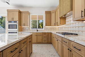 Kitchen featuring decorative backsplash, light stone counters, double oven, and stainless steel gas cooktop