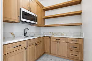 Kitchen with white microwave, open shelves, light stone counters, and light brown cabinets