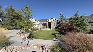 View of front facade with a front lawn, driveway, stucco siding, stone siding, and covered porch